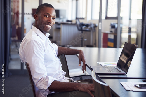 Young black man sitting at desk in office smiling to camera