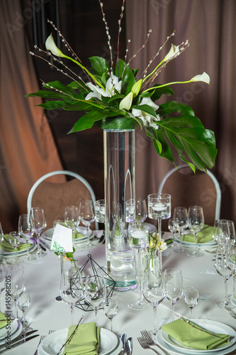 Closeup of table elegant served with green fabric napkins, small willow twigs and bouquet of flowers. Everything is eady for holiday celebration. Vertical color photography. photo