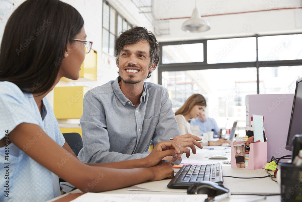 Man and young woman talking in a busy open plan office Man and young woman talking in a busy open plan office