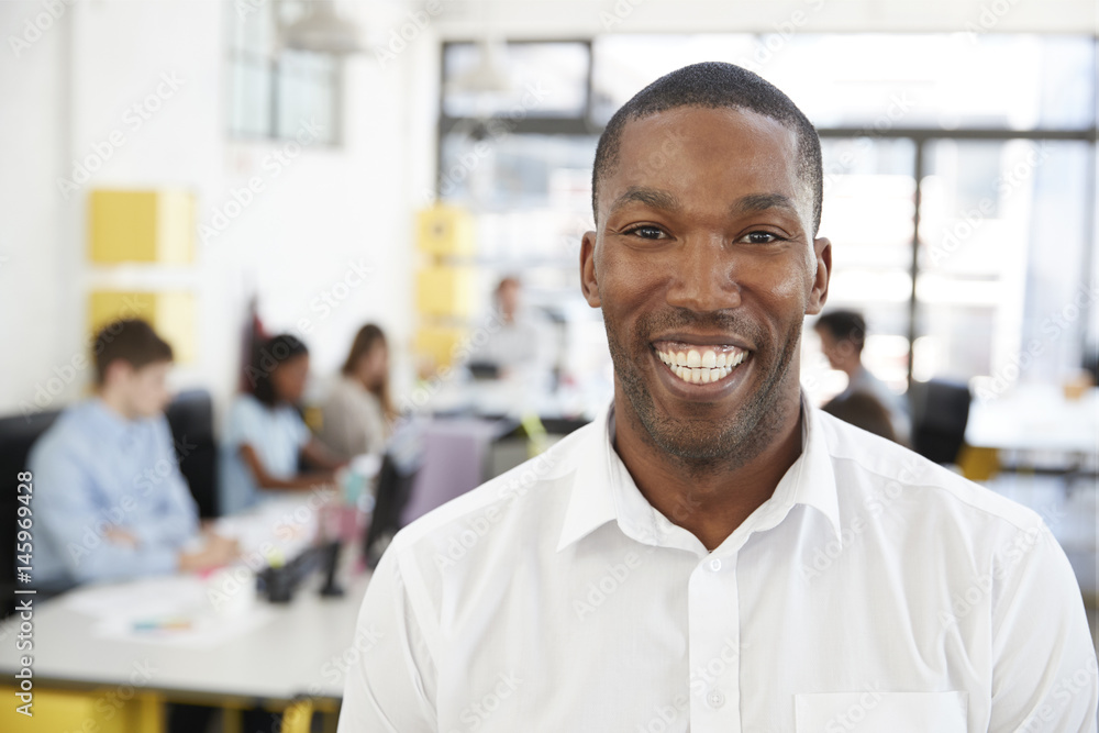 Mid adult black man smiling to camera in an open plan office Mid adult black man smiling to camera in an open plan office