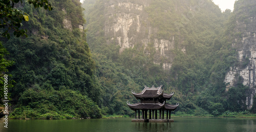 A scene of wooden bell tower floating on the water, surrounded by cliffs and jungle