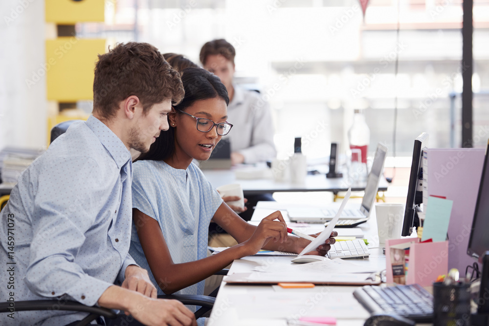 Young man and woman working together in an open plan office Young man and woman working together in an open plan office