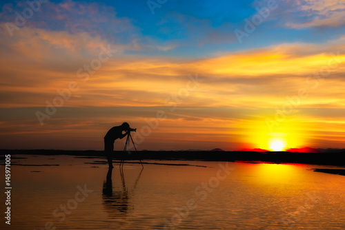 Silhouette Photographer take photo dramatic colorful sunset sky on beach in twilight.