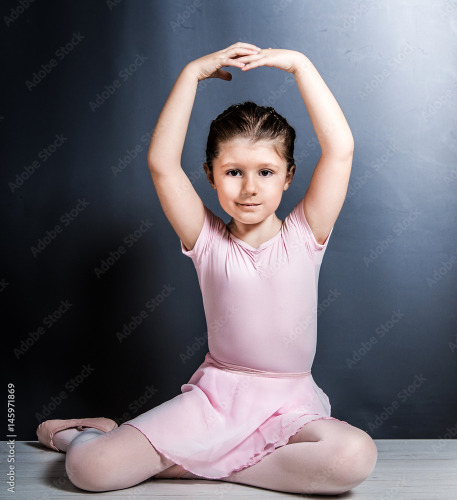 The classic ballet dancer in white tutu posing at ballet barre on studio  background. Young teen