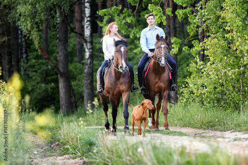 Young happy couple enjoying horse ride in a summer forest. 