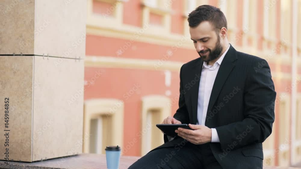 Young bearded businessman reading news on tablet computer during break in city street Young bearded businessman reading news on tablet computer during break in city street