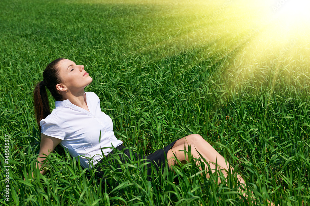 Business woman relaxing in green grass field outdoor under sun. Beautiful young girl dressed in suit resting, spring landscape, bright sunny day Business woman relaxing in green grass field outdoor under sun. Beautiful young girl dressed in suit resting, spring landscape, bright sunny day