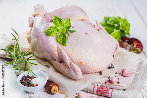 Raw whole chicken with herbs and spices on rustic wood background