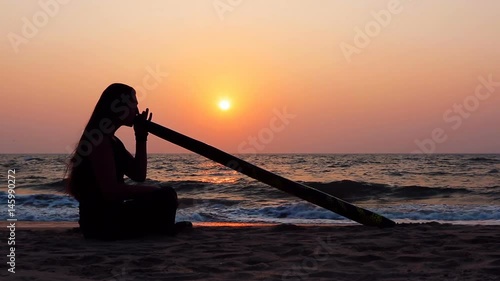 Didgeridoo playing. Male Silhouette with Didgeridu near Sea.