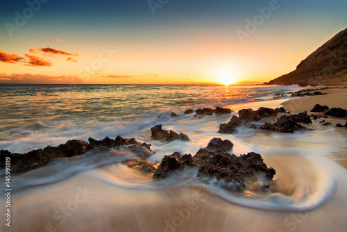 Slow exposure of waves washing around lava rocks on beach on west side of Oahu, Hawaii