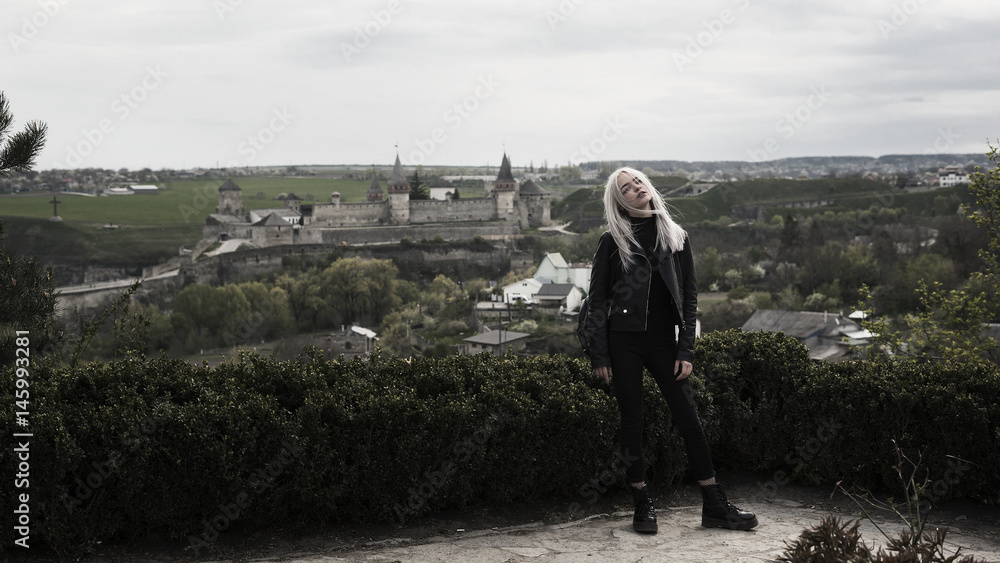 A girl in black clothes with white hair stands against the background of the old city with a castle. A girl in black clothes with white hair stands against the background of the old city with a castle.