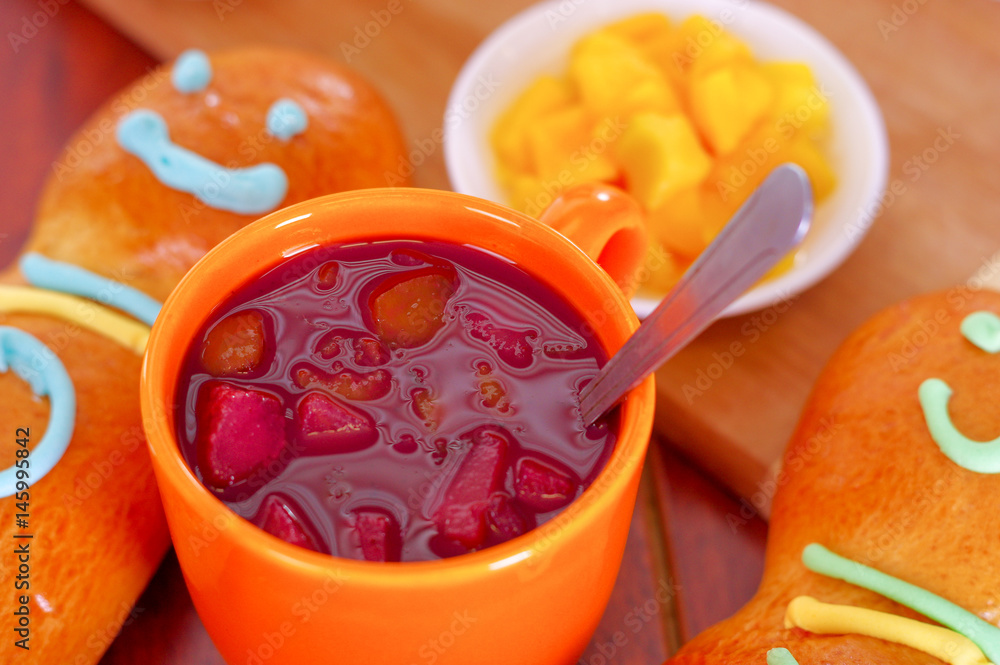 Elegant setup traditional tasty latin american guagua breads, colorful sugar decorations, orange cup with colada morada berry juice next to it, day of the dead concept Elegant setup traditional tasty latin american guagua breads, colorful sugar decorations, orange cup with colada morada berry juice next to it, day of the dead concept