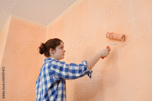 Young worker paint wall in a room to orange color using paint roller 