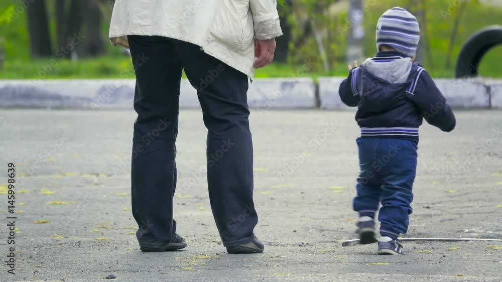 Grandmother comes with a small grandson along the street, rear view, slow motion