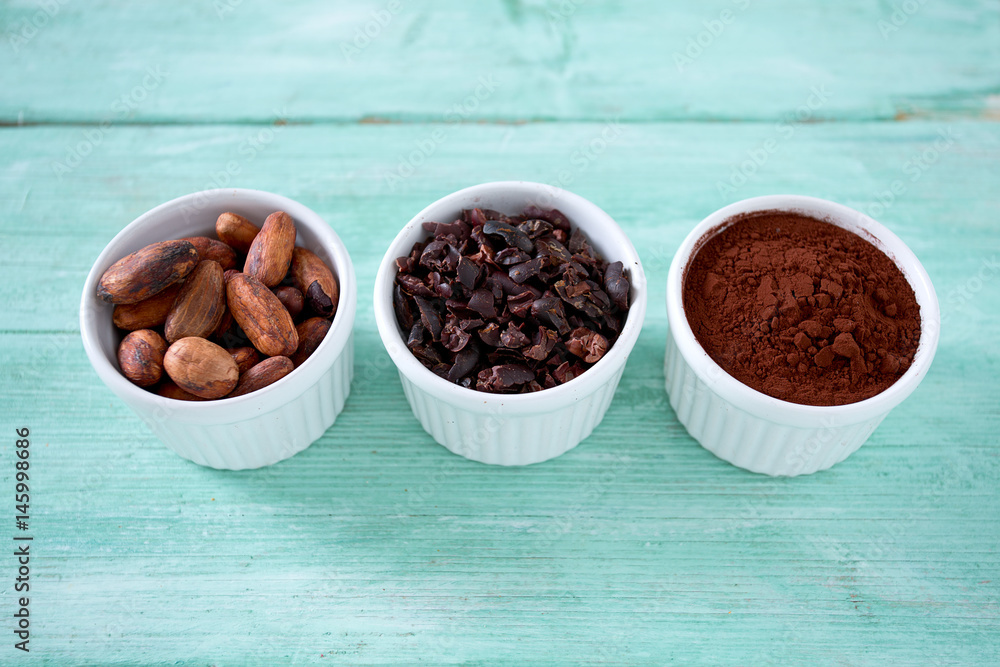 cocoa nibs, beans and powder on turquoise surface cocoa nibs, beans and powder on turquoise surface