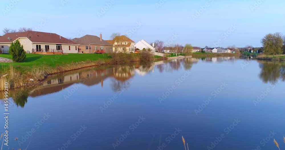 Beautiful neighborhood, houses reflected in mirror still pond, low aerial view.
Beautiful neighborhood, houses reflected in mirror still pond, low aerial view.