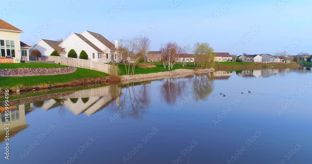 Beautiful neighborhood, houses reflected in mirror still pond, low aerial view.
Beautiful neighborhood, houses reflected in mirror still pond, low aerial view.
