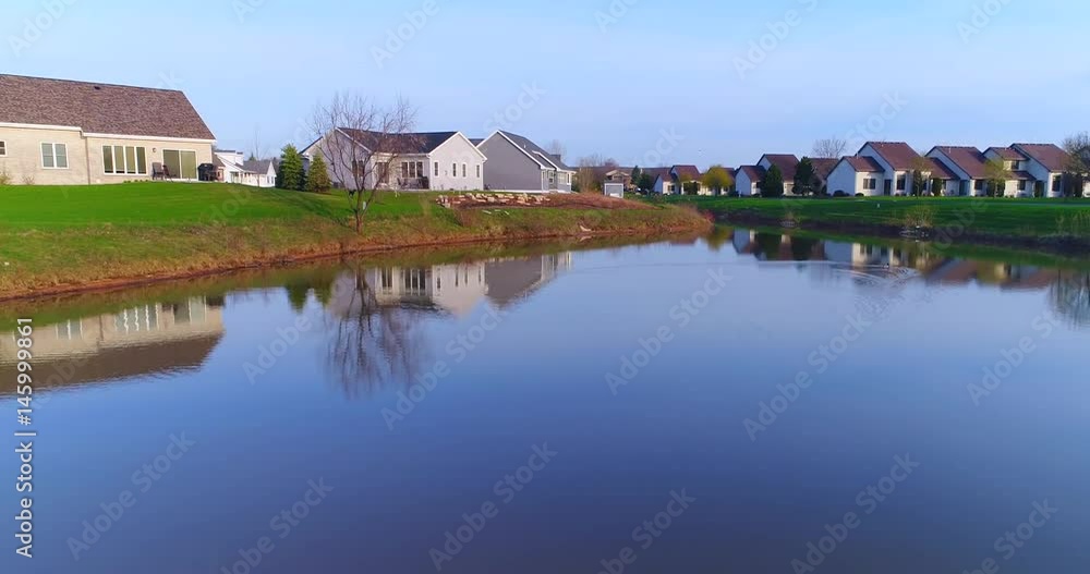 Beautiful neighborhood, houses reflected in mirror still pond, low aerial view.
Beautiful neighborhood, houses reflected in mirror still pond, low aerial view.