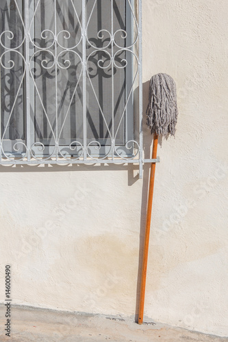 A mop stood outside a window of a house. Minimalist composition.