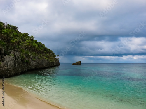 Roatan island Honduras. Landscape of a tropical blue turquoise clear ocean water and sandy beach. Blue dramatic cloudy sky in the background. Green palms on the reef rock.