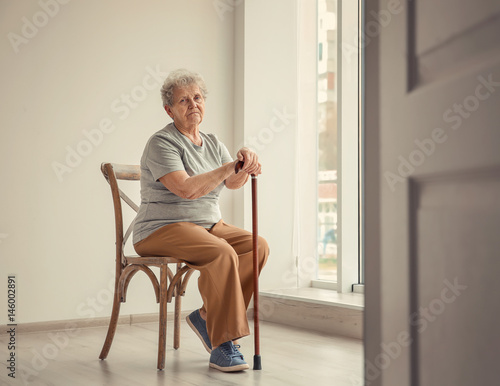 Fotografía Senior woman sitting on chair in empty room. Poverty concept