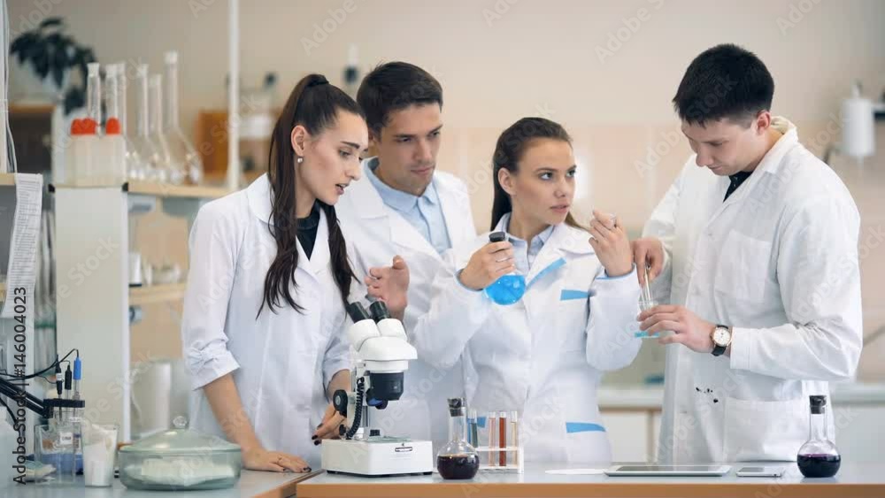 Scientists looking at beaker and discussing in laboratory Scientists looking at beaker and discussing in laboratory