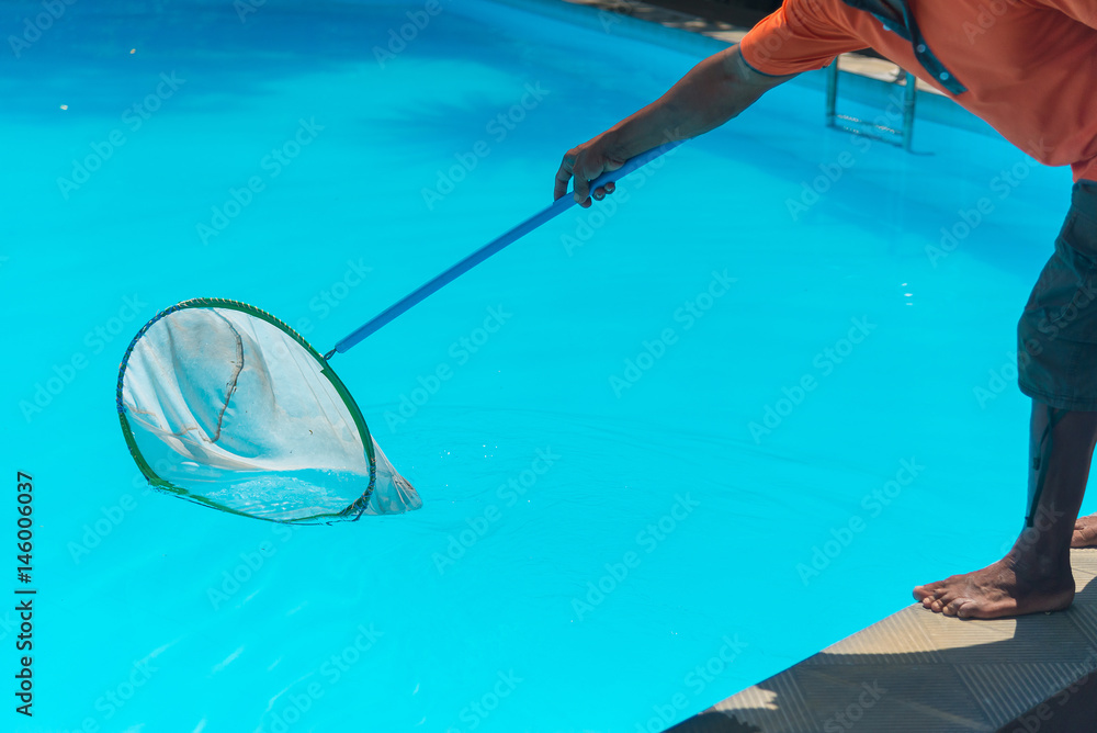 Man cleaning the blue swimming pool from leaves with cleaning net.