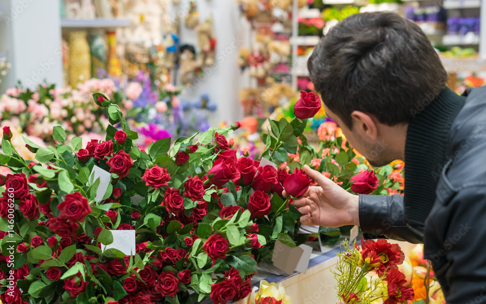 Handsome man choosing red roses at a florist shop for his girlfriend. Romantic present