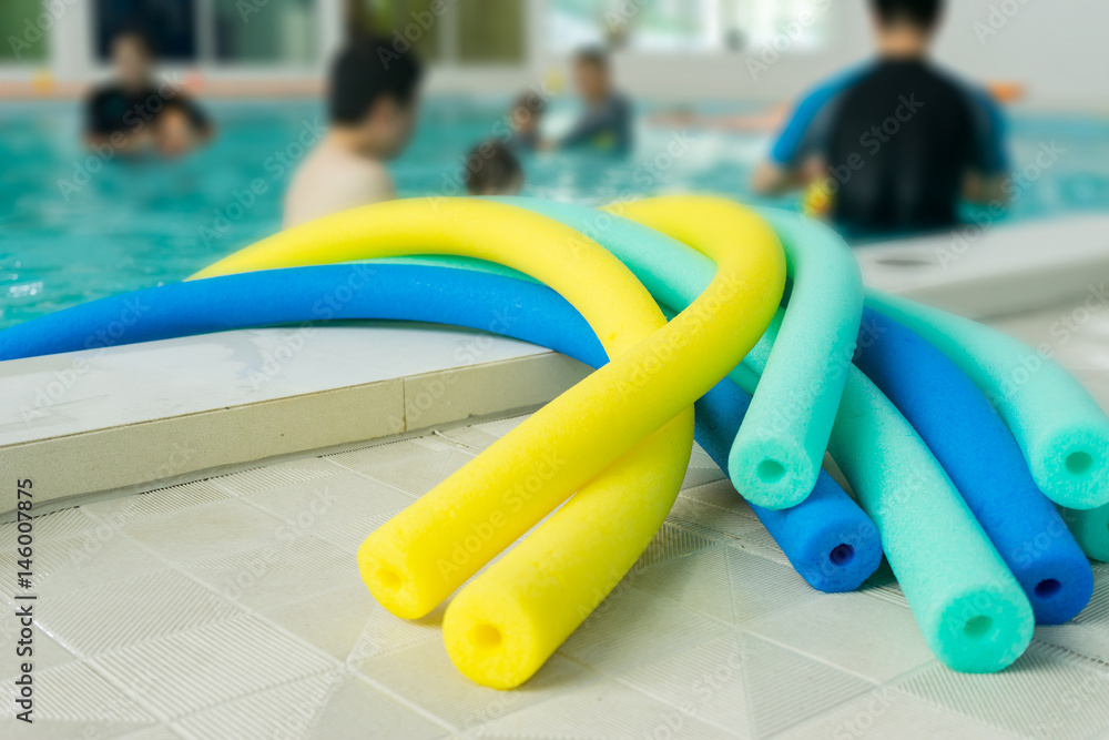 group of floating swim noodles in different colors for mother and farther teaching kid in swimming pool.selective focus