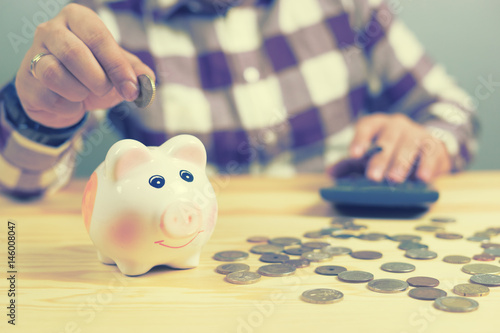money, home, finance and relationships concept -man with pig bank sitting on desk,Businessman putting coin into the piggy banks,vintage color morning light
