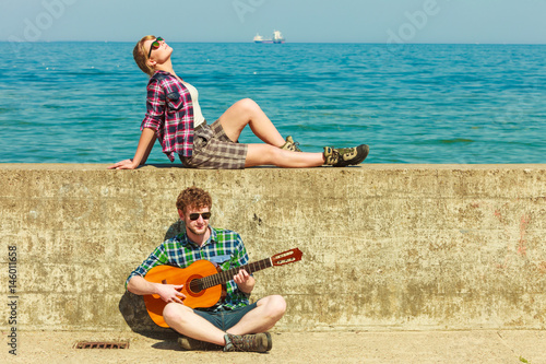 Young man playing guitar to his girlfriend by seaside photo