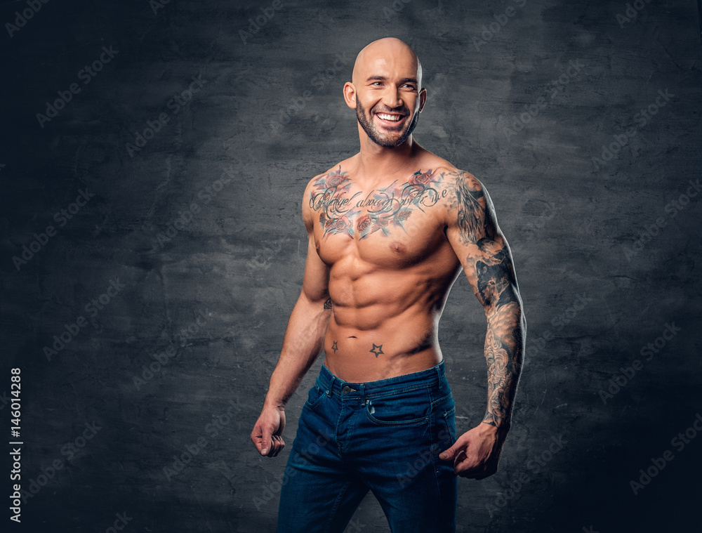 Fototapeta premium Shaved head, muscular male with tattoos on his torso over grey vignette background.