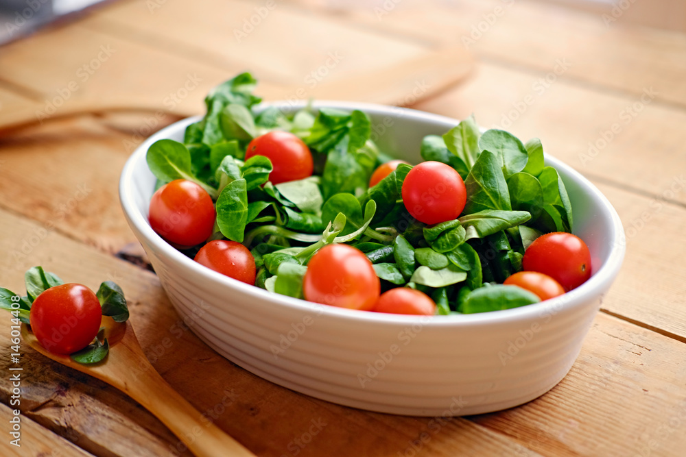 Cherry tomatoes and basil salad in a white cup on a wooden table.