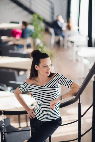 Portrait of beautiful successful brunette woman standing in her cafe and going upstairs while looking away.