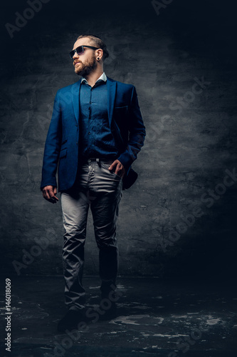 Full body studio portrait of stylish bearded male dressed in a suit and sunglasses.