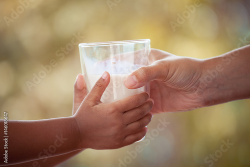 Woman hand giving glass of milk to child in vintage color tone