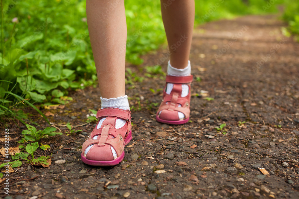 little girl legs in sandals walking on stony forest path