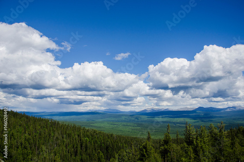 Sky and clouds above the green pine forest from top of mountain