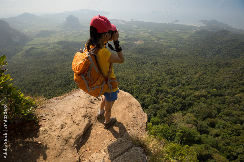 successful woman photographer taking photo on mountain peak cliff