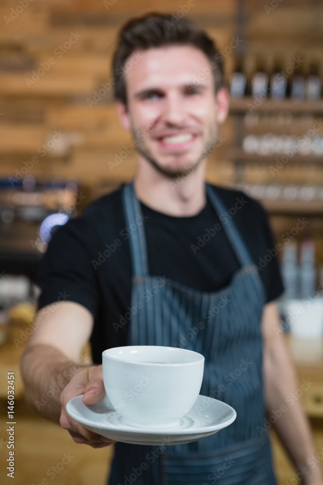 Smiling waiter offering cup of coffee at counter Smiling waiter offering cup of coffee at counter