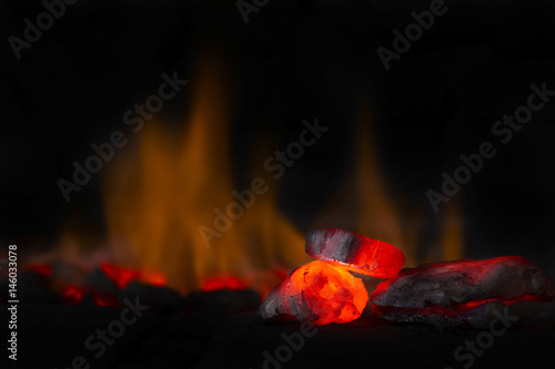 Red hot coal nugget in focus on dark background with flames. Background of raw coals with soft focus exclusion with color and temperature.