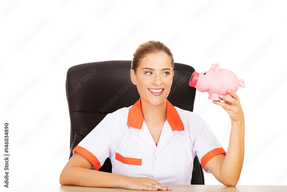 Smile doctor sitting behind the desk and holding a piggybank Smile doctor sitting behind the desk and holding a piggybank