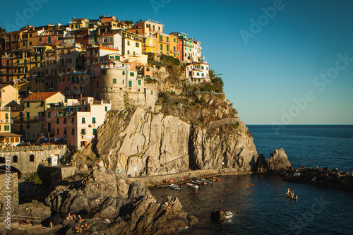 Village of Manarola, Cinque terre, at sunset landscape. A small boat in the sea. Soft orange-yellow sunset light on the landscape.