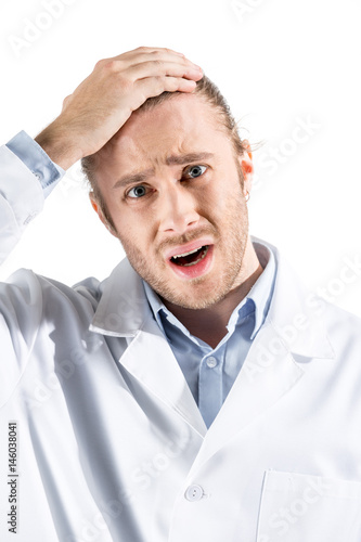 portrait of shocked young doctor in white coat looking at camera isolated on white