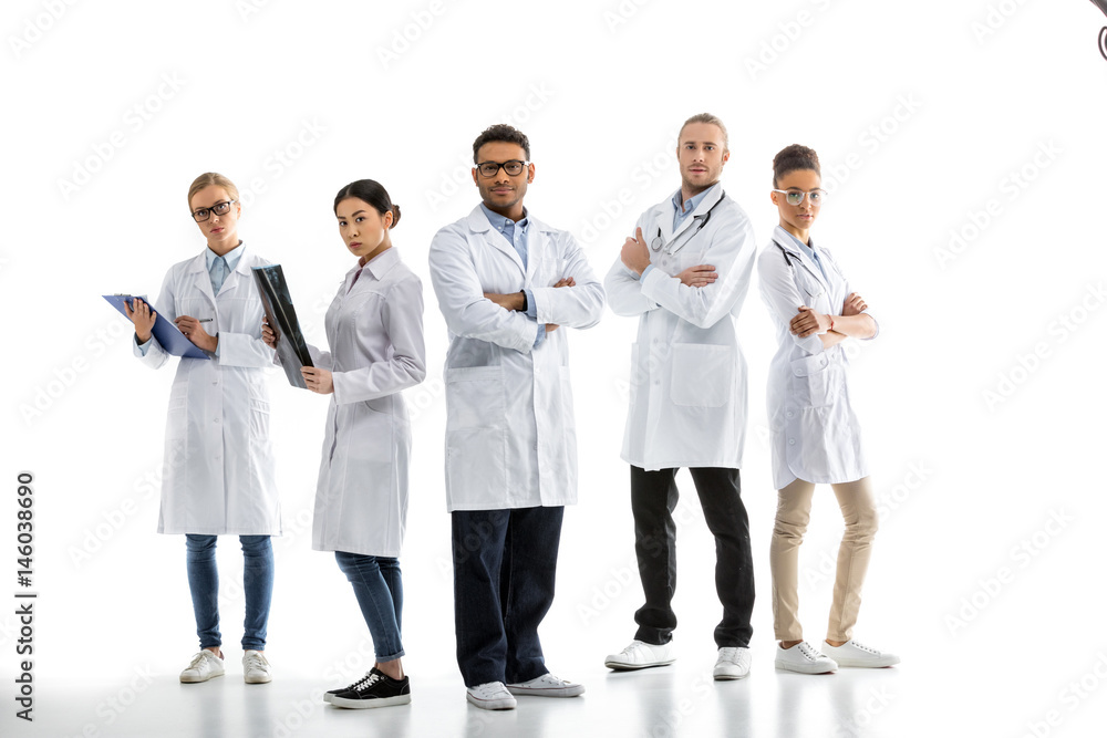 Group of young confident professional doctors in white coats standing isolated on white Group of young confident professional doctors in white coats standing isolated on white