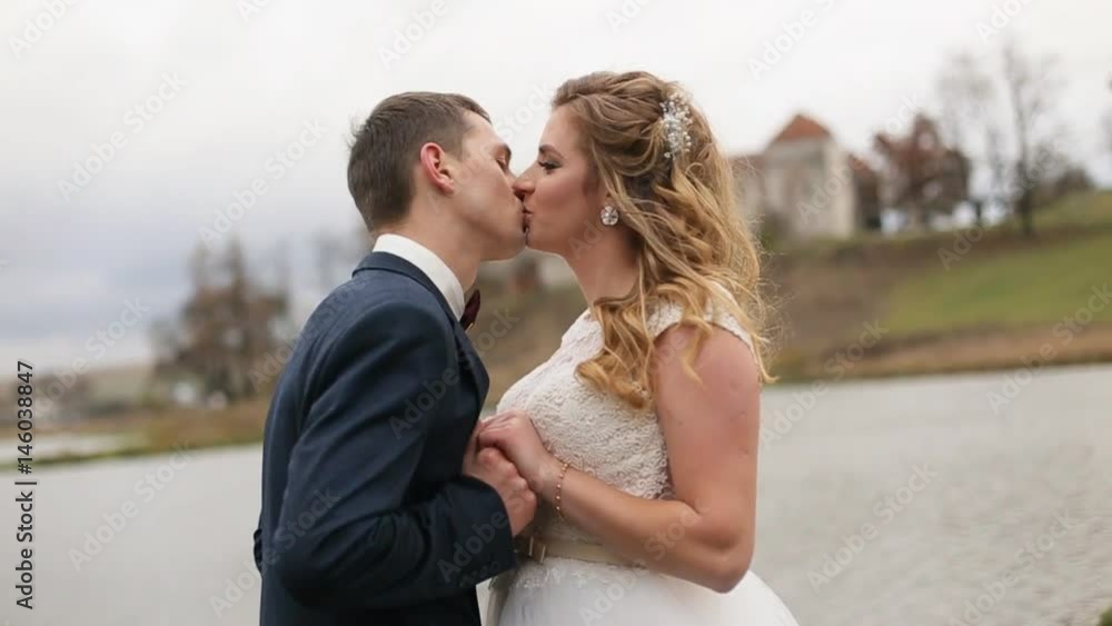 Happy young bride and groom kissing each other near the lake. Wedding couple Happy young bride and groom kissing each other near the lake. Wedding couple