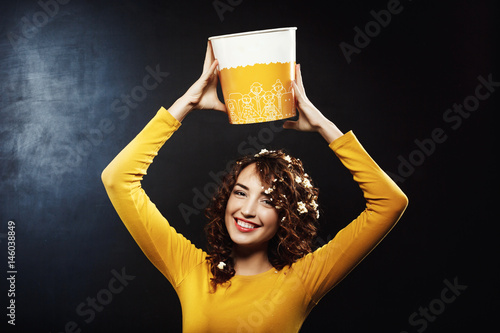 Nice woman in yellow sweatshirt holding popcorn bucket up, smiling  photo