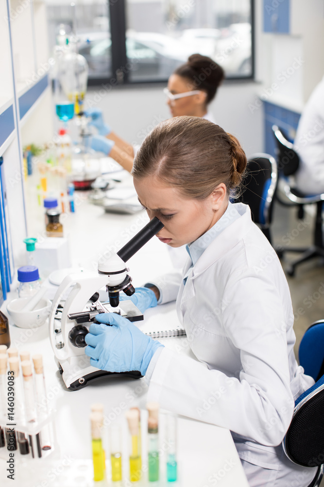 Focused young scientist working with microscope in research laboratory Focused young scientist working with microscope in research laboratory