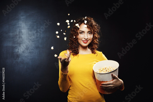 Nice young woman throwing popcorn up in the air smiling photo