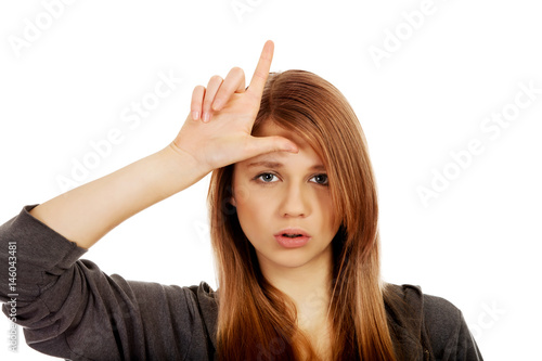 Obraz na plátne Teenage woman makes loser sign on her forehead
